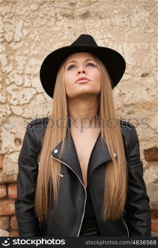 Blonde young woman with black hat and leather jacket looking up