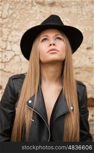 Blonde young woman with black hat and leather jacket looking up