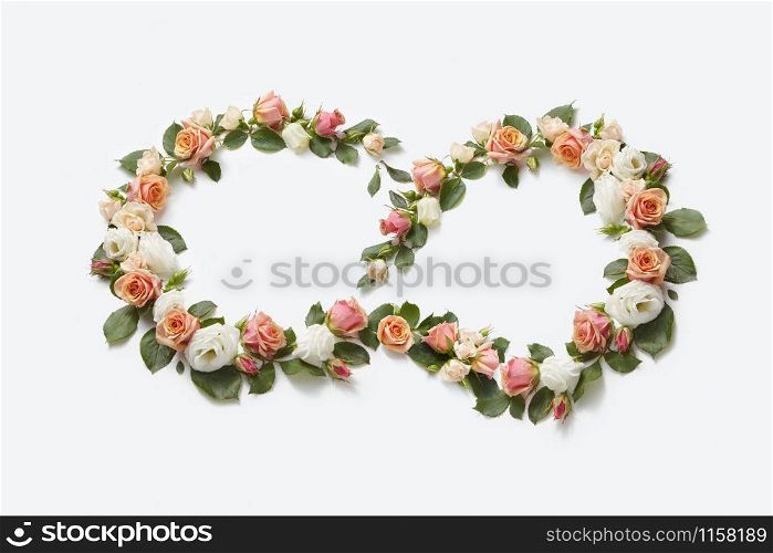 Blooming corner flowers wearth from coral roses with green leaves on a light grey background, copy space. Flat lay. Valentine&rsquo;s Day concept.. Flowers roses wreath in the shape of figure eight.