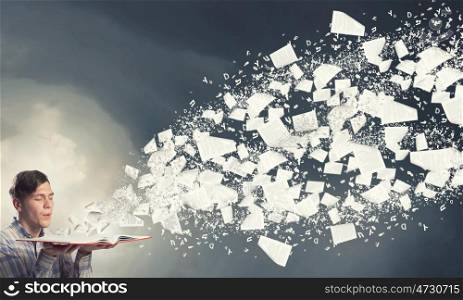Blow dust from pages. Young businessman with opened book in hands blowing on pages