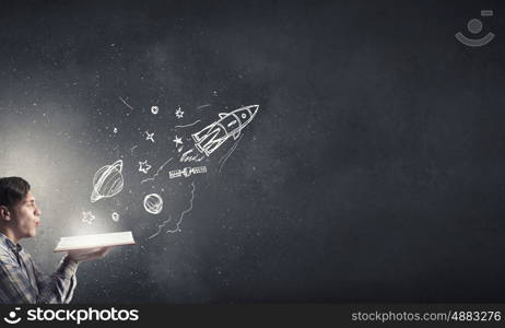 Blow dust from pages. Young businessman with opened book in hands blowing on pages