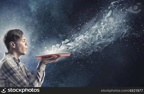 Blow dust from pages. Young businessman with opened book in hands blowing on pages