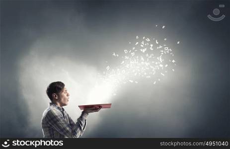 Blow dust from pages. Young businessman with opened book in hands blowing on pages