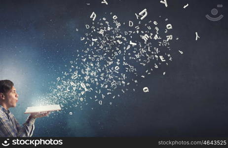 Blow dust from pages. Young man with opened book in hands blowing on pages