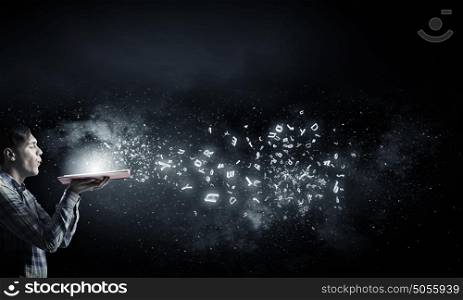Blow dust from pages. Young man with opened book in hands blowing on pages