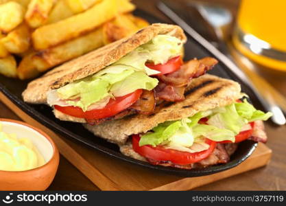 BLT (bacon, lettuce, tomato) wholewheat pita sandwich with French fries and mayonnaise in the front (Selective Focus, Focus on the front of the two pita stuffings)