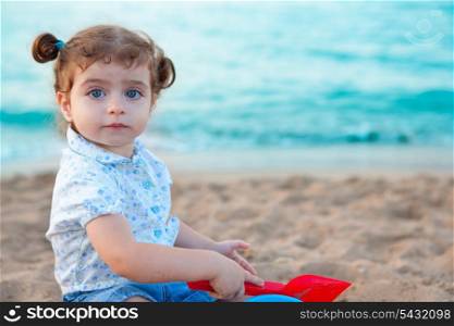 Blu eyes brunette toddler girl playing with sand in beach at mediterranean