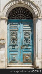Blue aged Tunisian wooden door with arch and ornament. Culture and architecture of Tunisia