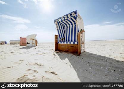 Blue and white striped roofed wicker beach chair in backlight. White sandy tropical beach in hot summer sunshine. Travelling and summer vacation concept.