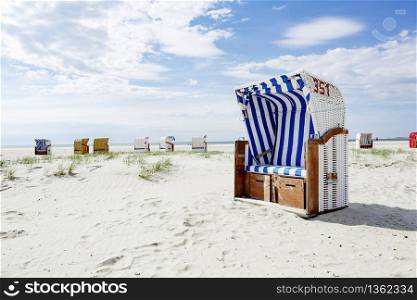 Blue and white striped wooden beach chair or bench on a white sandy tropical beach in hot summer sunshine in a travel and vacation concept