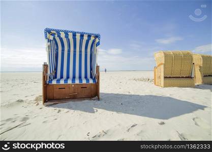 Blue and white striped wooden beach chair or bench on white sandy tropical beach in hot summer sunshine. Travelling and summer vacation concept.
