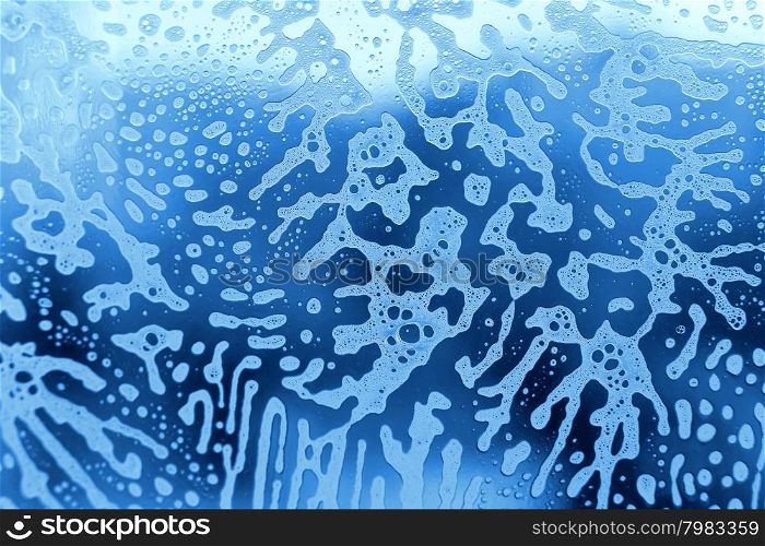 Blue background with natural soap foam pattern on the glass