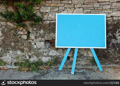 Blue blank signboard standing near an old stone wall, copy space for your text