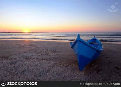 Blue boat on beach at sunrise