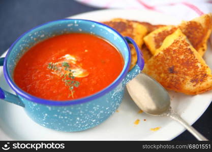 Blue bowl of tomato soup with fresh thyme and a grilled cheese sandwich cut into triangles