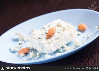 Blue cheese and almonds on a plate on a wooden background. Selective focus. Blue cheese and almonds on plate on wooden background