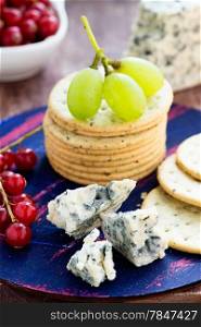 Blue cheese and crackers with fruits on wooden board, selective focus