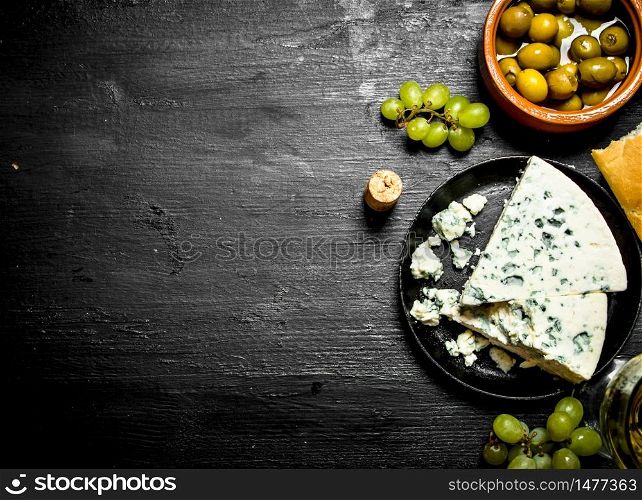 Blue cheese, olives and white grapes. On a black wooden background.. Blue cheese, olives and white grapes.