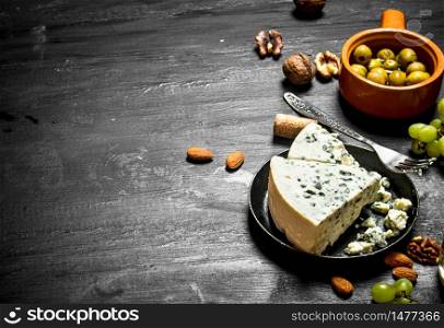 Blue cheese, olives and white grapes. On a black wooden background.. Blue cheese, olives and white grapes.
