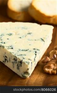 Blue cheese with walnut and bread slices on wooden plate, photographed with natural light (Selective Focus, Focus one third into the cheese)