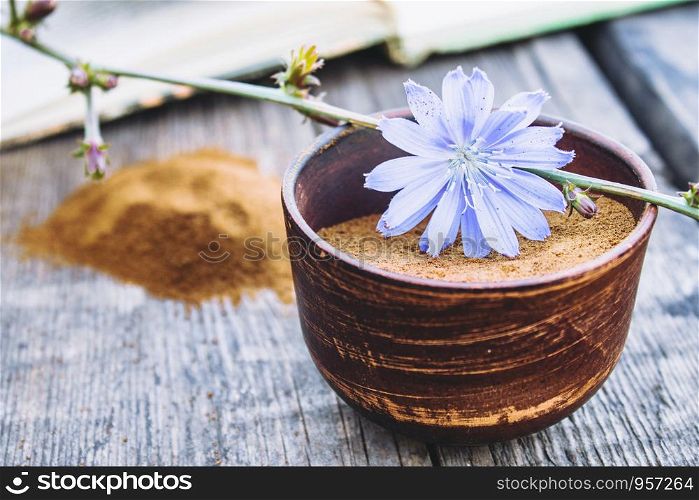 Blue chicory flower and a bowl of instant chicory powder on an old wooden table. Chicory powder. The concept of healthy eating a drink. Coffee substitute.. Blue chicory flower and a bowl of instant chicory powder on an old wooden table. Chicory powder. The concept of healthy eating a drink.