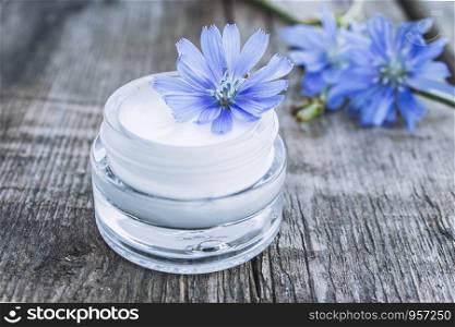 Blue chicory flower and face cream in a glass jar on an old wooden table. Health concept. Spa. Blue chicory flower and face cream in a glass jar on an old wooden table. Health concept.