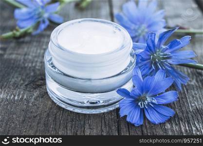 Blue chicory flower and face cream in a glass jar on an old wooden table. Health concept. Spa. Blue chicory flower and face cream in a glass jar on an old wooden table. Health concept.