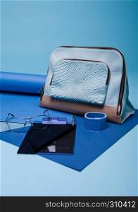 Blue color fashion style still life setup on blue background with bag glasses and pen