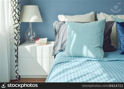 Blue color scheme bedding and white table lamp with natural light from a window