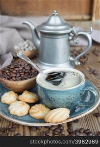 Blue cup of black coffee, cookies and coffee pot surrounded by linen cloth, sugar pieces and coffee beans on old wooden table
