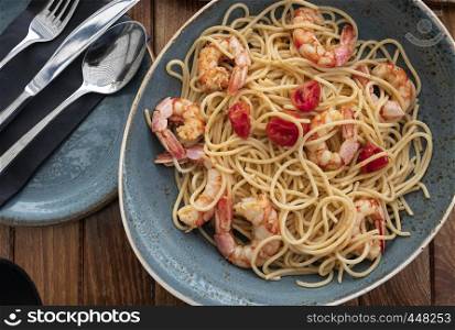 blue dish of spaghetti with prawns and pieces of tomatoes