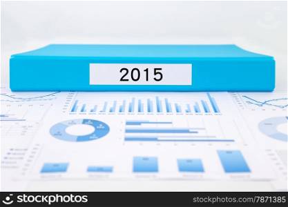 Blue document binder with year number 2015 place on graphs and charts of financial analysis reports