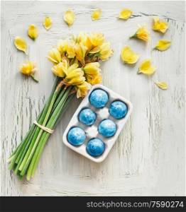Blue Easter egg in holder with yellow daffodils flowers bunch on white shabby chick background. Top view