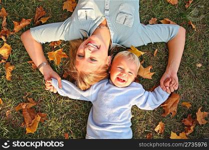 blue-eyed blond lies with the son on the earth at the park in autumn
