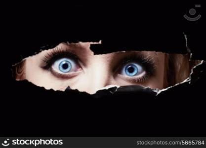 Blue eyes of a young woman peeping through a hole