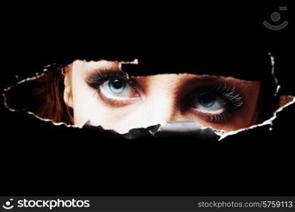 Blue eyes of young woman peeping through a hole closeup