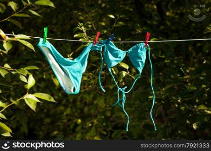 Blue female swimsuit drying on clothesline at garden