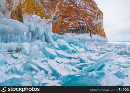 Blue frozen water covered with snow and icicles at rocky island in Lake Baikal, Russia