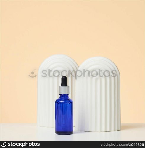 blue glass bottle with pipette stands on a beige background. Cosmetics SPA branding. Packaging for gel, serum, advertising and product promotion