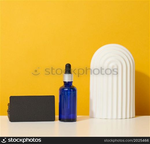 blue glass bottle with pipette stands on a white table. Cosmetics SPA branding. Packaging for gel, serum, advertising and product promotion, mock up