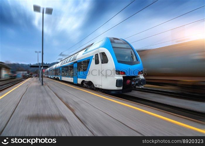Blue high speed train in motion on the railway station at sunset. Fast modern intercity train and blurred background. Railway platform. Railroad in Slovenia. Commercial and passenger transportation. Blue high speed train in motion on the railway station at sunset
