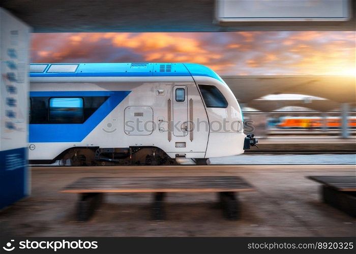 Blue high speed train in motion on the railway station at sunset. Fast modern intercity train and blurred background. Railway platform. Railroad. Commercial and passenger transportation. Side view. Blue high speed train in motion on the railway station at sunset