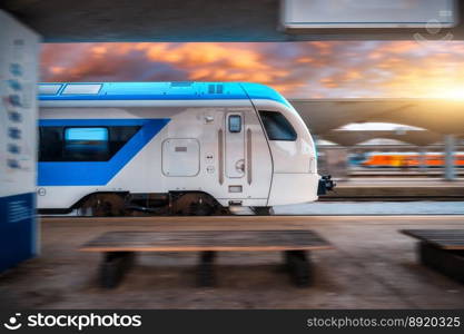 Blue high speed train in motion on the railway station at sunset. Fast modern intercity train and blurred background. Railway platform. Railroad. Commercial and passenger transportation. Side view. Blue high speed train in motion on the railway station at sunset