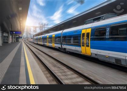 Blue high speed train in motion on the railway station at sunset. Fast modern intercity train and blurred background. Railway platform. Railroad in Austria. Commercial and passenger transportation. Blue high speed train in motion on the railway station at sunset
