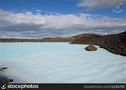 Blue lagoon with rocky coastline under a bright blue clouded sky