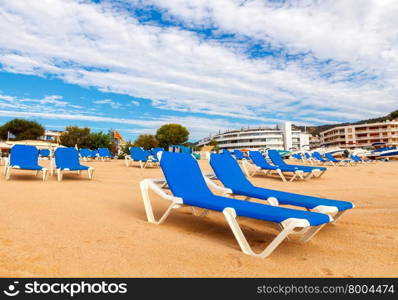 Blue lounge chairs at the beach of Tossa de Mar in the early morning.