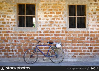 Blue mountain bike parked leaning against a brick wall with two wired windows