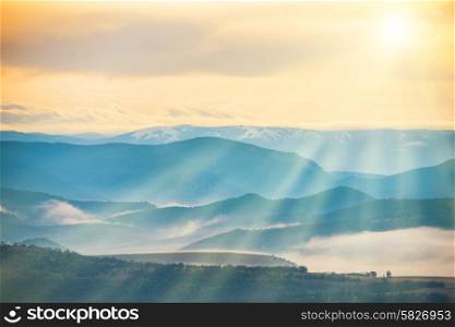 Blue mountains covered with mist against sunset. Bright sun shining on the sky