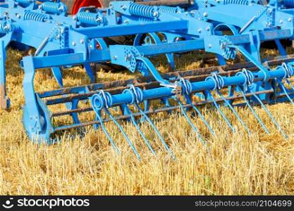 Blue multirow cylindrical metal harrow for tractor hitch for agricultural processing of fields. Closeup, selective focus, copy space.. A multi-row cylindrical metal harrow in blue against a harvested yellow field in sunlight. Closeup.