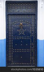 Blue painted wooden door with gold colored decoration in the medina of Asilah, Morocco